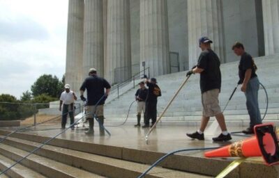 Crew of six workers washing wide granite steps at a large government building with stone columns