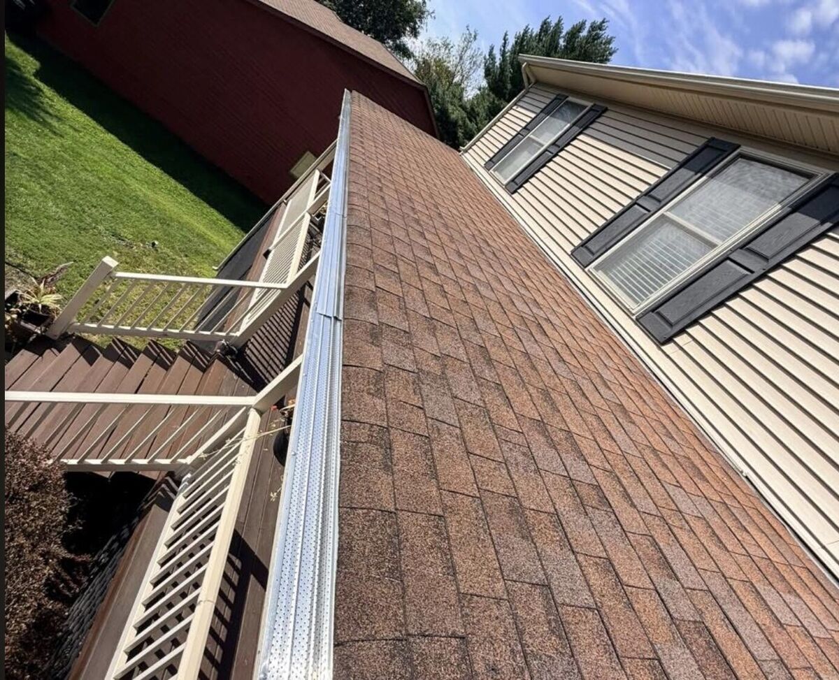 Finished gutter guard installation running the full length of a shingle roof edge above a deck