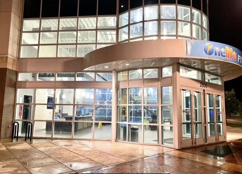 Fitness club entrance with a glass curtain wall and freshly washed concrete sidewalk at night