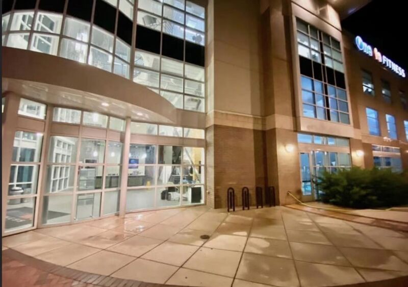 Fitness club exterior at night with wet, freshly cleaned sidewalk and entry paving