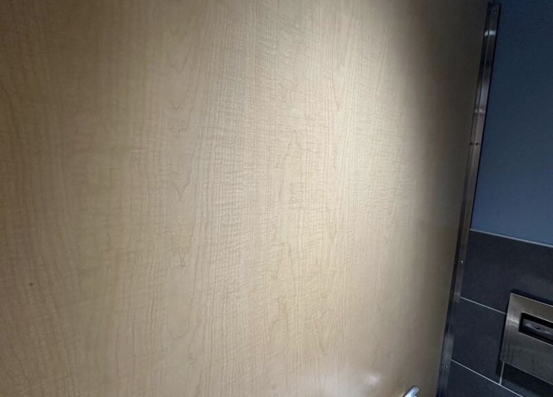 The same wood-grain restroom wall panel after cleaning, with the marker fully removed and the grain clean