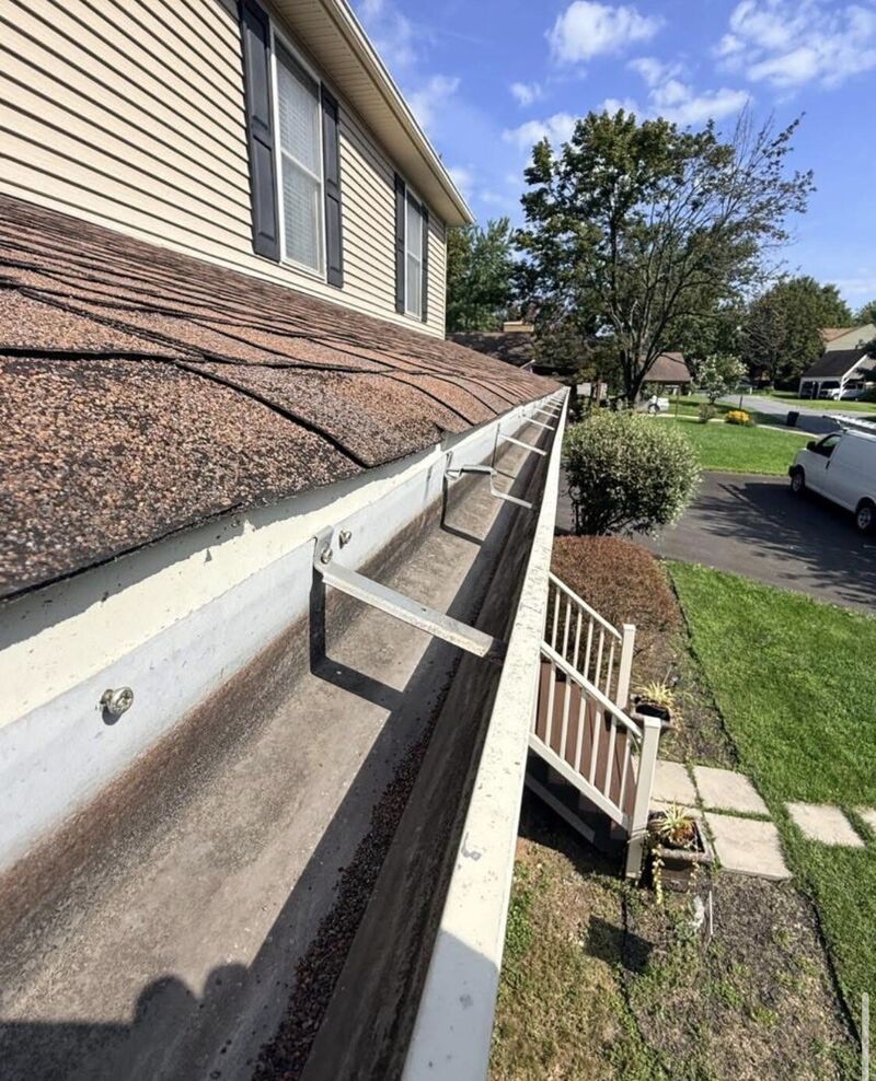 Open gutter run along a shingle roof edge holding shingle granules and debris before cleaning