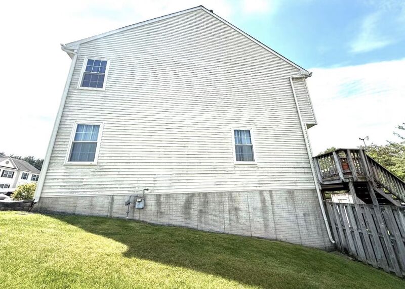 Two-story house gable with cream vinyl siding streaked gray-green with algae before soft washing