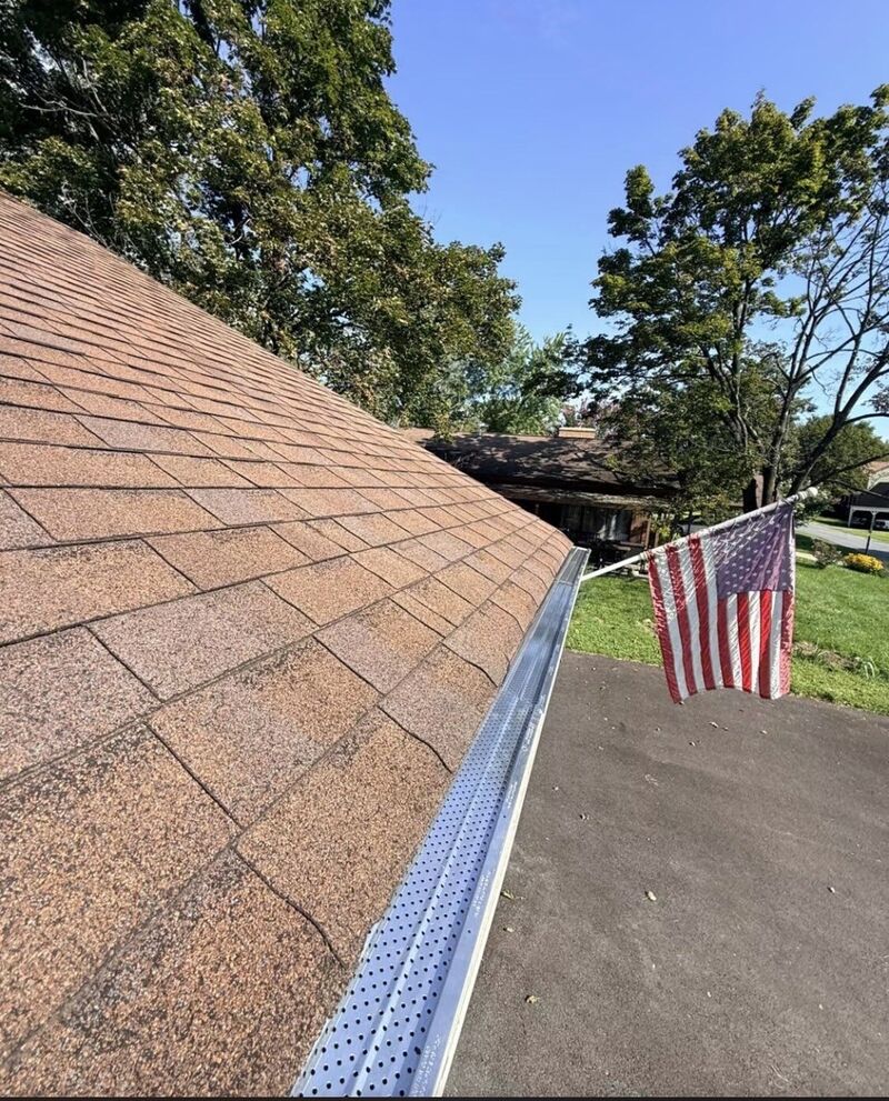 Perforated metal gutter guard installed along a shingle roof edge
