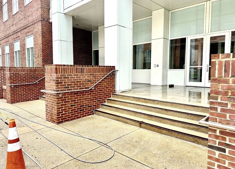 Institutional building entrance with brick knee walls and concrete steps being cleaned, hose and safety cone in place